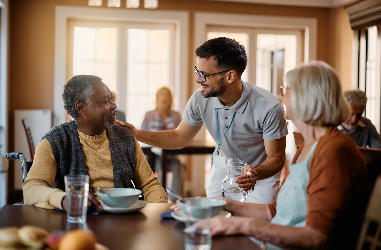 A group of seniors have breakfast in a care community while being assisted by trained staff
