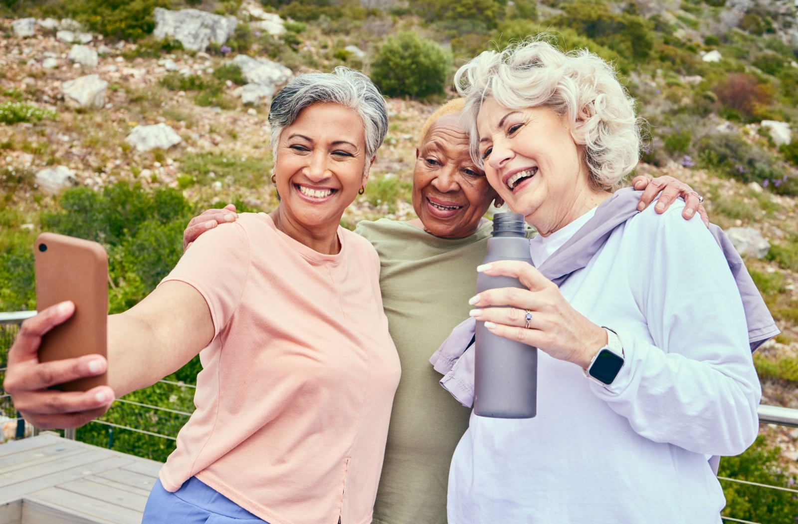 3 senior friends take a happy selfie along a summer hiking trail.