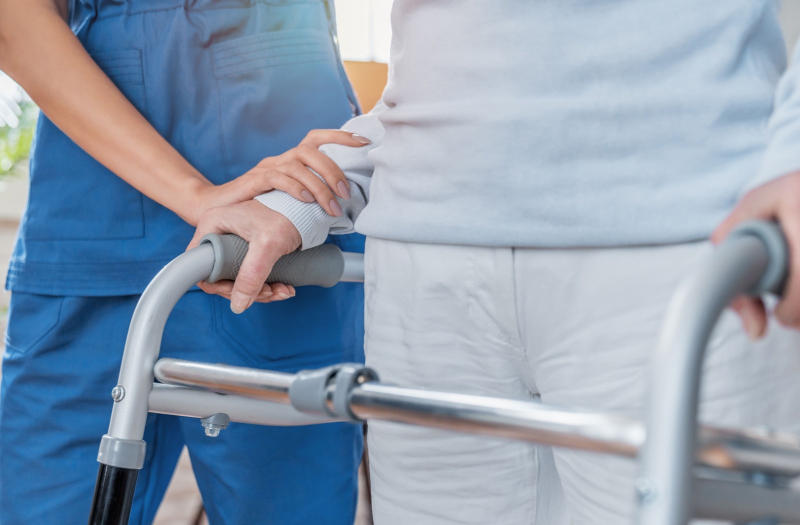 A nurse in skilled nursing care at a senior living community helps a senior resident walk in their walker while recovering from surgery