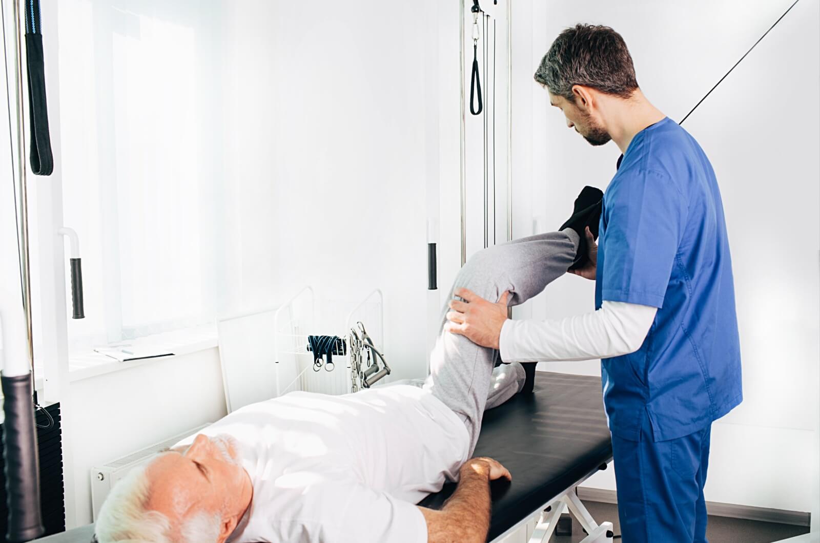 A healthcare professional helping an older adult whose lying down perform a knee lift on their right knee.
