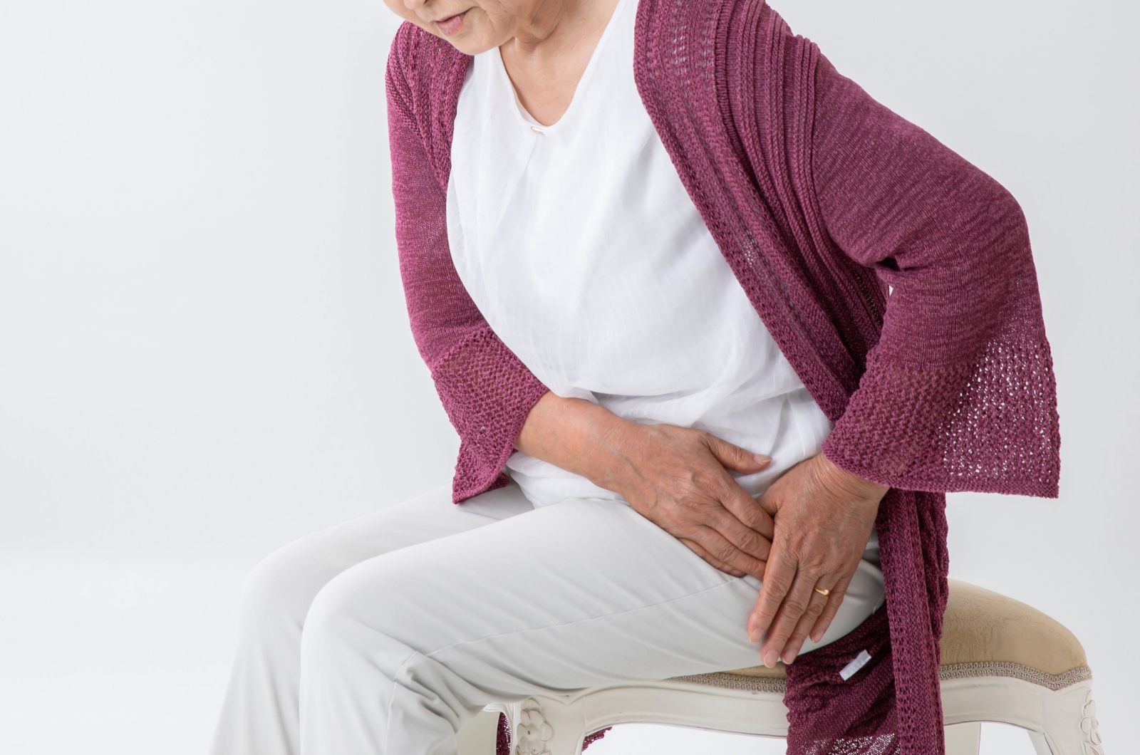 A close-up image of an older adult holding their left hip with both hands due to pain.