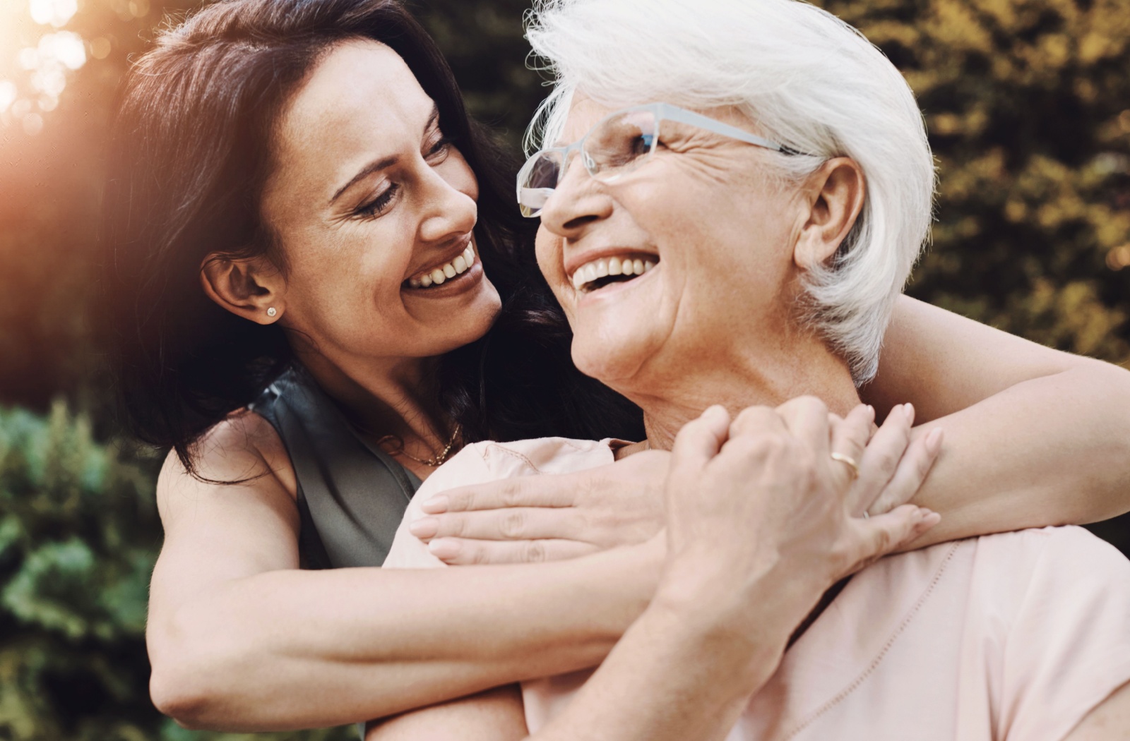 An adult embraces their senior parent joyously on a stroll in the community garden.