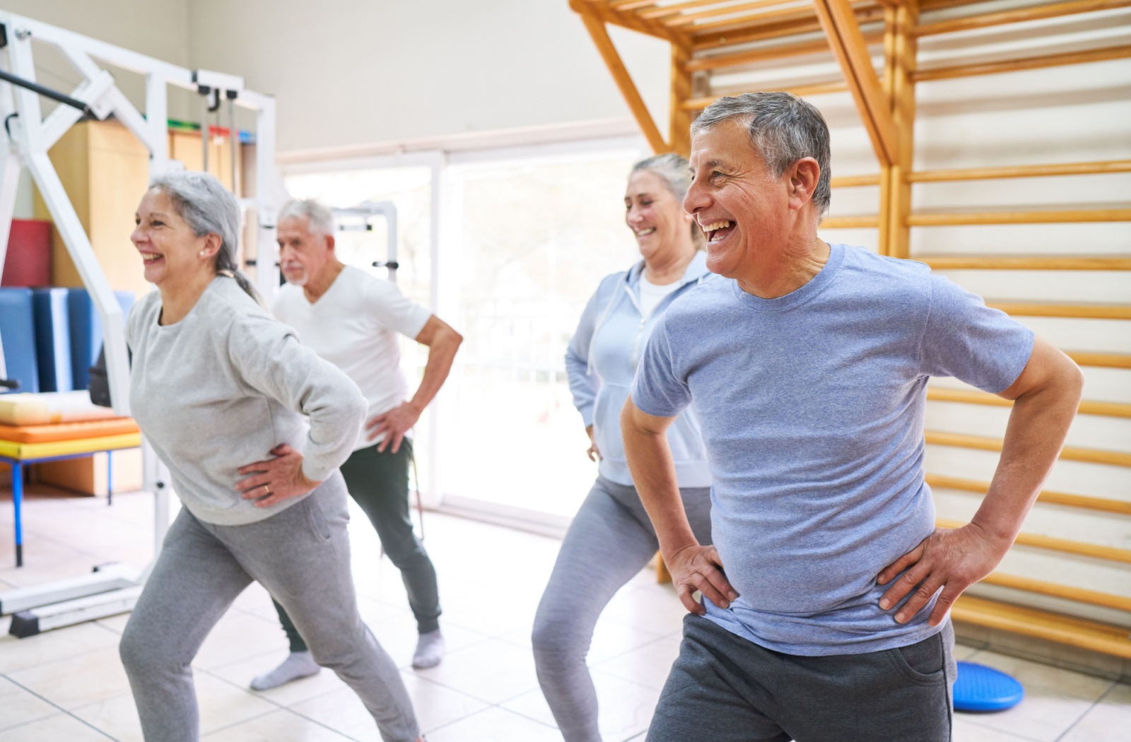 A group of 4 seniors smiling while doing posture exercises in an indoor studio.