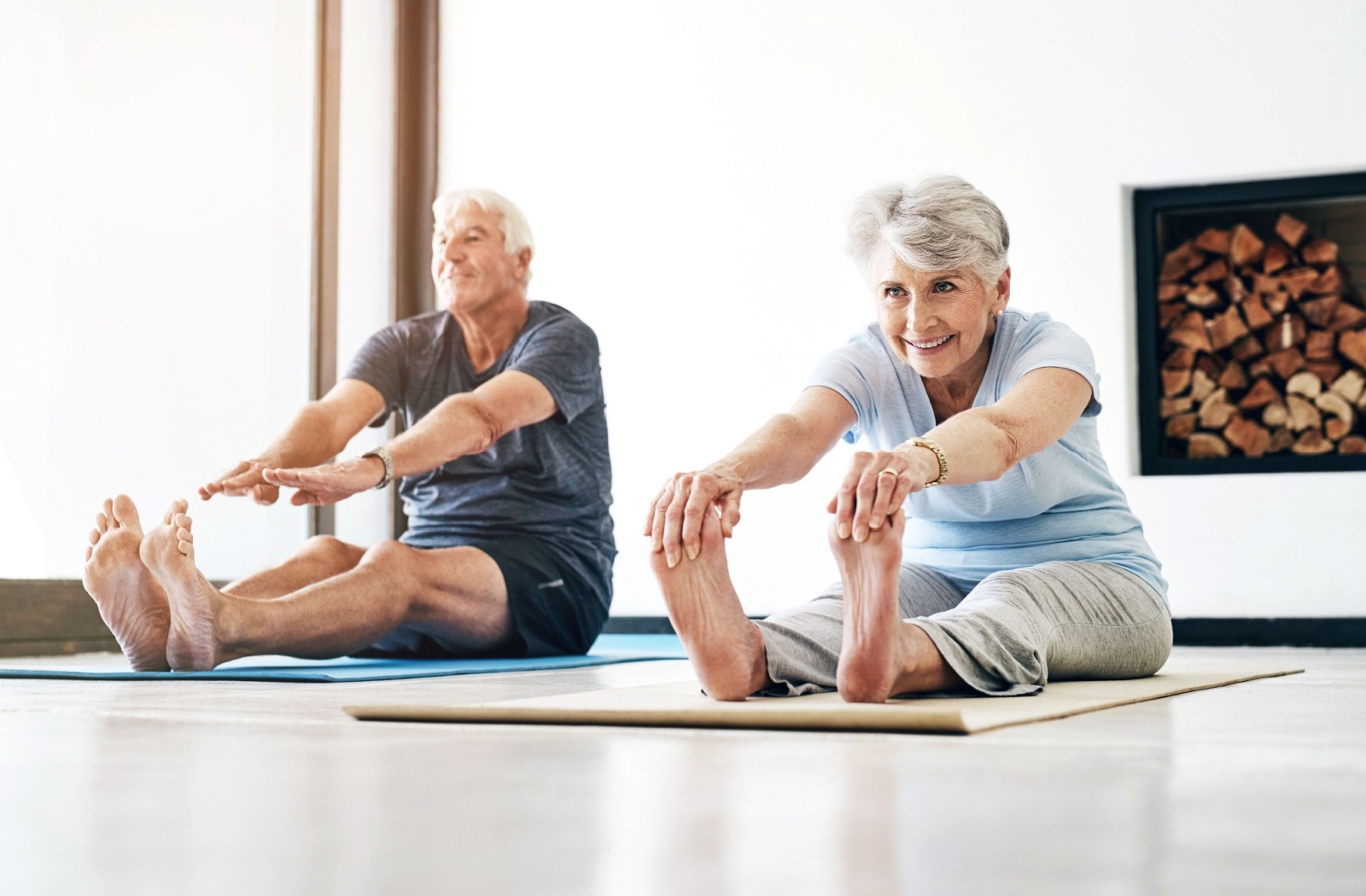 Two older adults stretching to touch their toes during an exercise class in senior living.