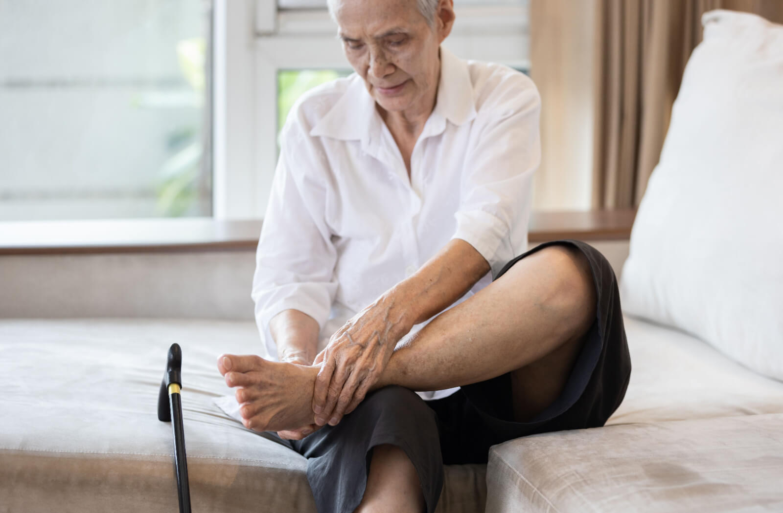An older adult sits on their bed to rub their ankle and reduce swelling