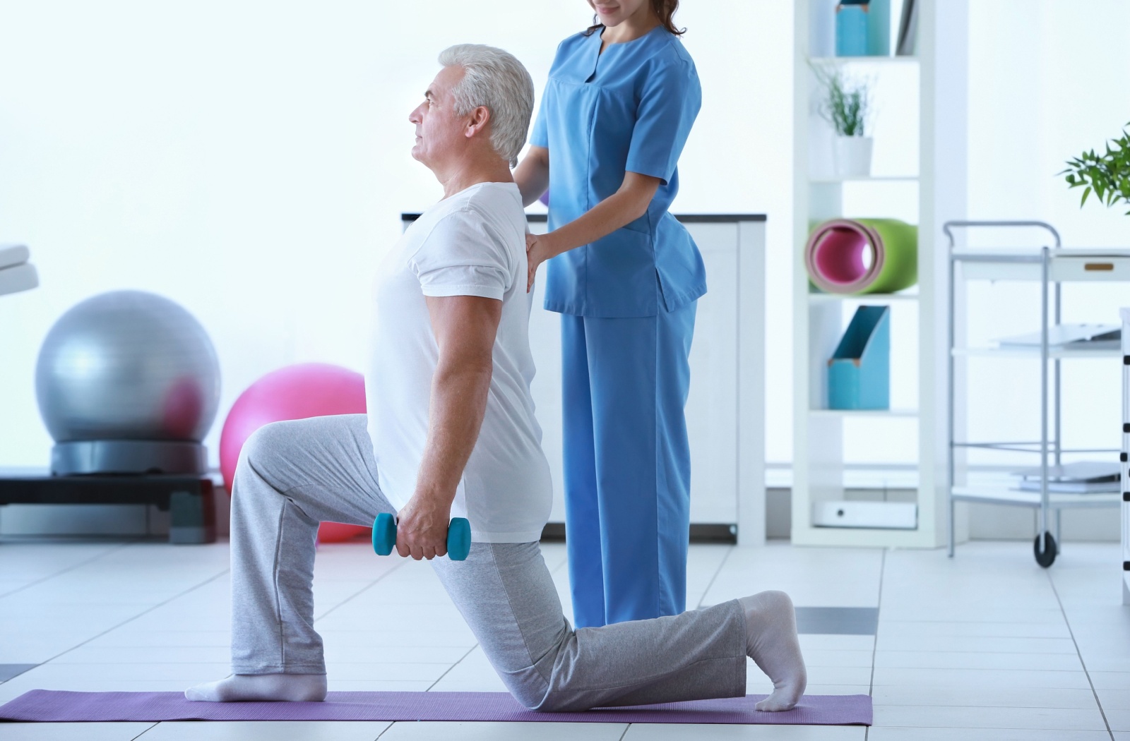 A physiotherapist helps a senior with their posture while performing strength-training exercises to help with bone strength
