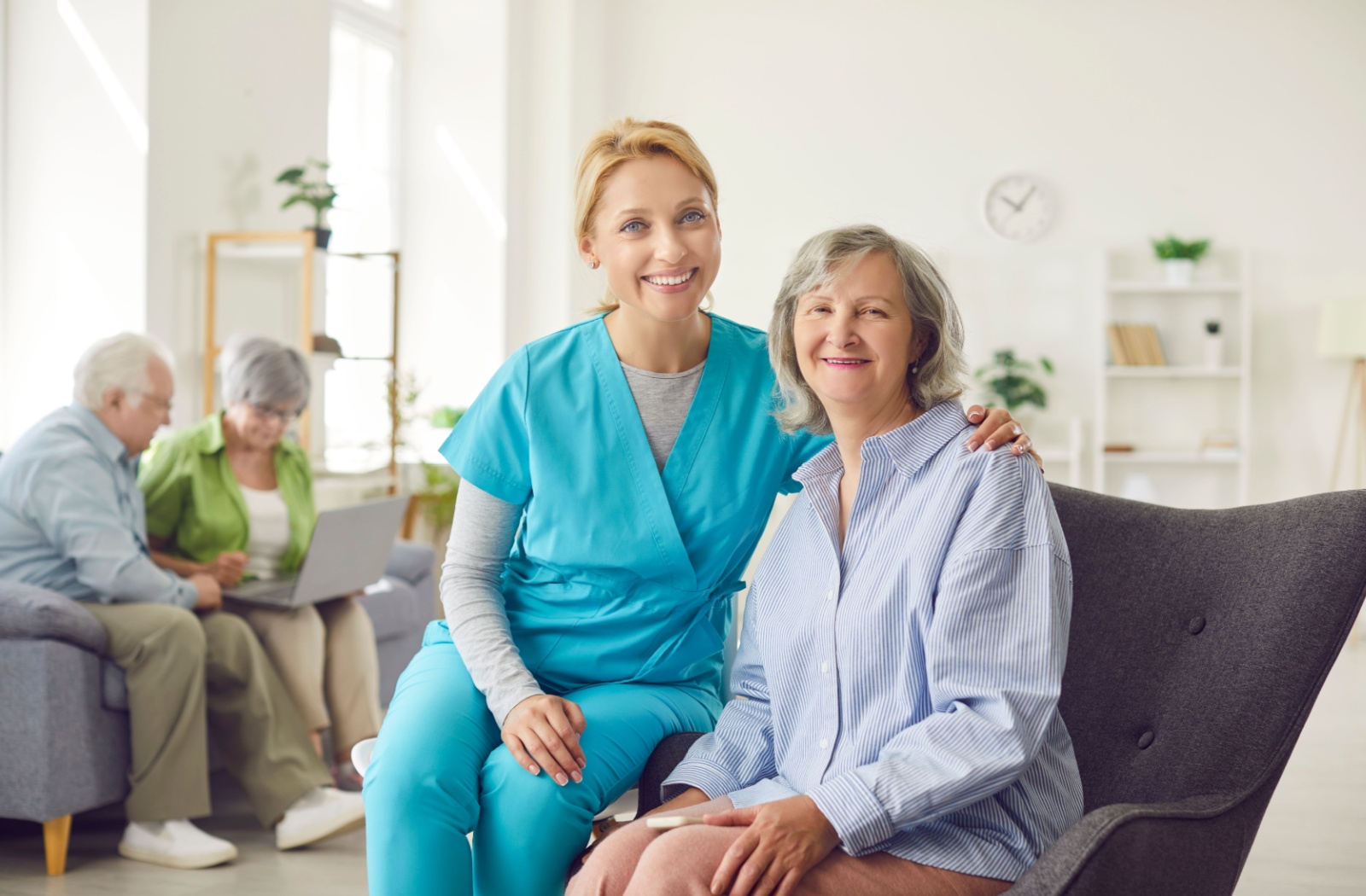 An older adult smiles beside a caregiver while sitting in a common lounge of senior living in respite care