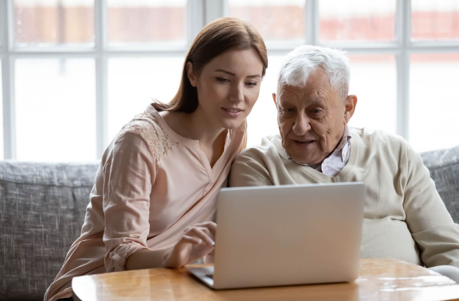An adult child and their older parent use a laptop on the couch to research respite care options
