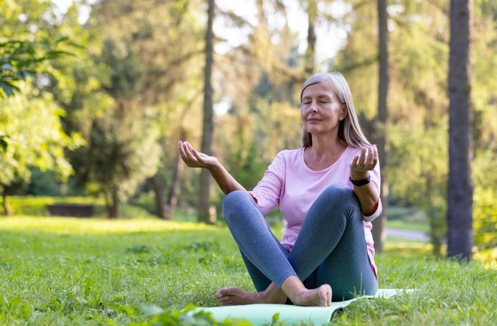 A senior meditates on a yoga mat while sitting outside on a summer day.